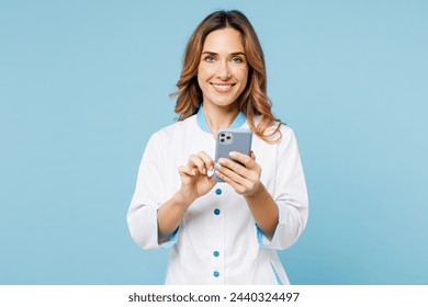 Female smiling happy doctor woman wears white medical gown suit work in hospital clinic office hold in hand use mobile cell phone isolated on plain blue background studio. Health care medicine concept - Powered by Shutterstock