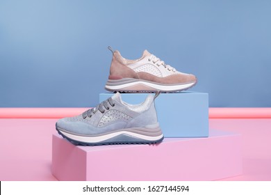 Female Sneakers Of Different Colors, But Of The Same Model, Stand On A Pink, Blue Stand From The Studio. Promotional Photo