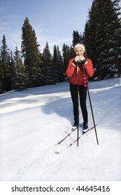 Female Snow Skiier Smiling, Standing In The Snow Leaning On Ski Poles.  Vertically Framed Shot.