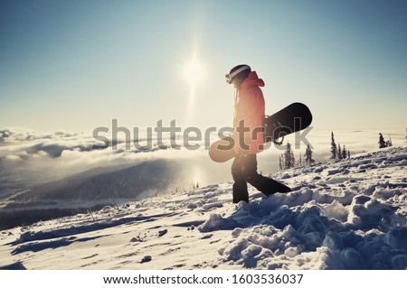 Female snowboarder holding snowboard standing on mountain slop, preparing to snowboarding. Sunny winter day in ski resort