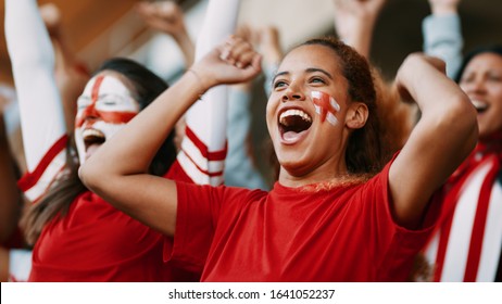Female soccer fans of England watching and celebrating their team's victory. English female spectators enjoying after a win at stadium.