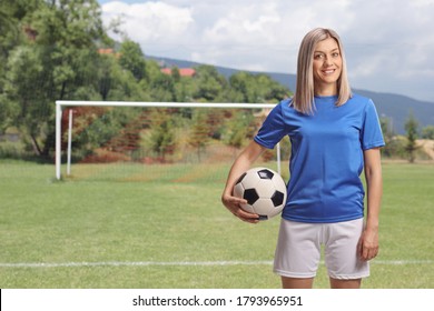 Female soccer player holding a ball under arm and standing on a football pitch - Powered by Shutterstock