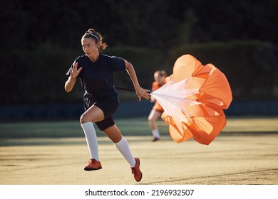 Female soccer player running with parachute during sports training at the stadium. - Powered by Shutterstock