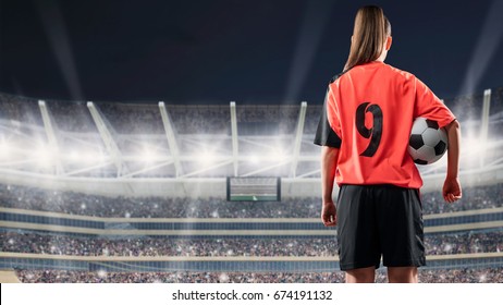 female soccer player standing with the ball against the crowded stadium at night - Powered by Shutterstock