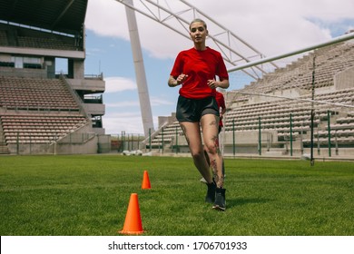 Female soccer players practicing on the field. Women soccer uniform running between the cones arranged on field. - Powered by Shutterstock