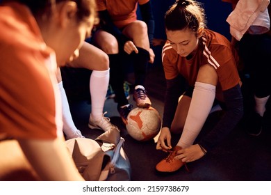 Female soccer team dressing up for sports match in locker room. Focus is on woman tying shoelace.  - Powered by Shutterstock