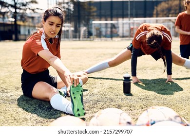 Female soccer team warming up for sports training on playing field. Focus is on woman stretching her leg. - Powered by Shutterstock