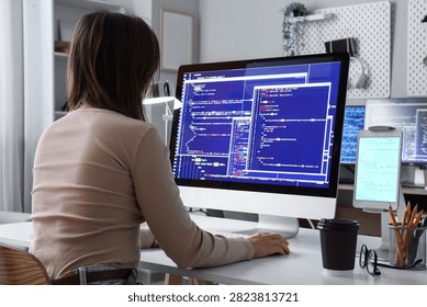 Female software developer coding on a desktop computer with multiple screens in a modern home office setting