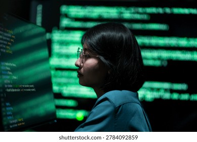 A female software engineer working with digital programming code and cybersecurity data displayed on computer screens in a modern office environment. The scene represents information technology, software development, and data security operations.