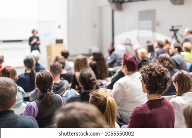 Female speaker giving presentation in lecture hall at university workshop. Audience in conference hall. Rear view of unrecognized participant in audience. Scientific conference event. - Shutterstock ID 1055550002
