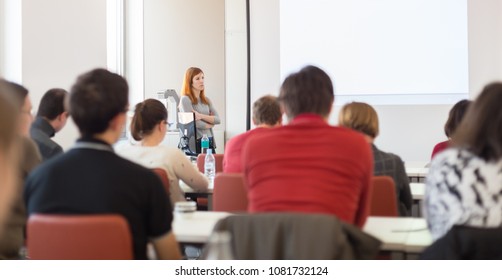 Female speaker giving presentation in lecture hall at university workshop. Audience in conference room. Rear view of unrecognized participant in audience. Scientific conference event.