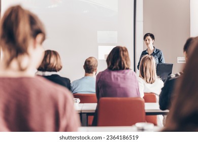 Female speaker giving presentation in lecture hall at university workshop . Participants listening to lecture and making notes. Scientific conference event. - Shutterstock ID 2364186519