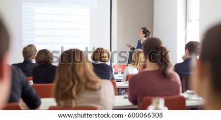 Female speaker giving presentation in lecture hall at university workshop . Participants listening to lecture and making notes. Scientific conference event.