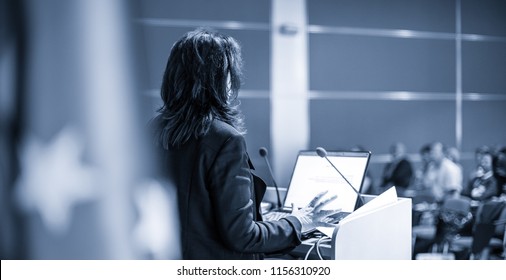 Female speaker giving a talk on corporate Business Conference. Audience at the conference hall. Business and Entrepreneurship event. Black and white, blue toned image. - Shutterstock ID 1156310920