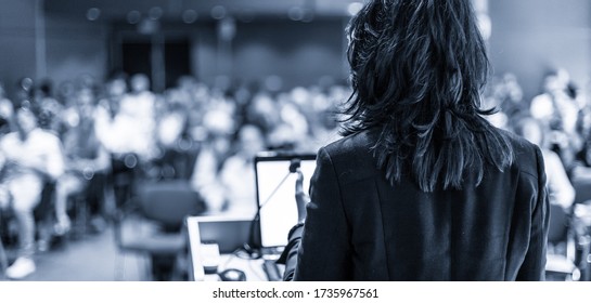 Female Speaker Giving A Talk On Corporate Business Conference. Unrecognizable People In Audience At Conference Hall. Business And Entrepreneurship Event. Black And White, Blue Toned Image.