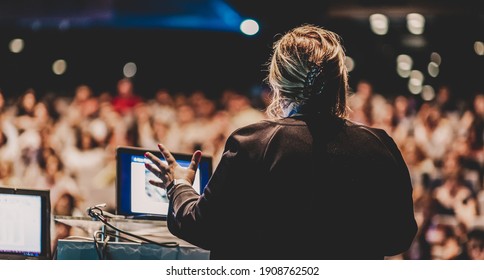 Female Speaker Giving A Talk On Corporate Business Conference. Unrecognizable People In Audience At Conference Hall. Business And Entrepreneurship Event.