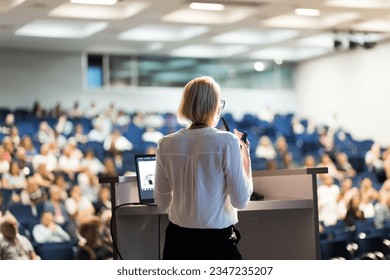 Female speaker giving a talk on corporate business conference. Unrecognizable people in audience at conference hall. Business and Entrepreneurship event - Powered by Shutterstock