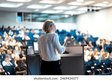 Female speaker giving a talk on corporate business conference. Unrecognizable people in audience at conference hall. Business and Entrepreneurship event