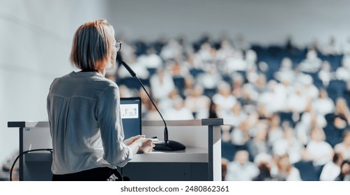 Female speaker giving a talk on corporate business conference. Unrecognizable people in audience at conference hall. Business and Entrepreneurship event - Powered by Shutterstock