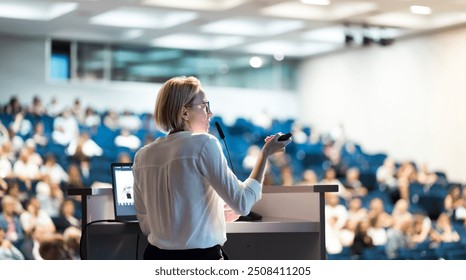 Female speaker giving a talk on corporate business conference. Unrecognizable people in audience at conference hall. Business and Entrepreneurship event - Powered by Shutterstock