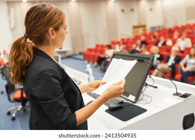 Female speaker holding document at podium during business seminar in convention center - Powered by Shutterstock