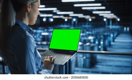 Female It Specialist Using Chroma Key Laptop In Data Center. Big Server Farm Cloud Computing Facility With Maintenance Engineer Working With Green Screen Computer.