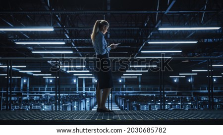 Female IT Specialist Using Tablet Computer in Data Center, Walking on a Bridge Overlooking Gigantic Server Farm Cloud Computing Facility. Succesful Businesswoman, e-Business Entrepreneur.
