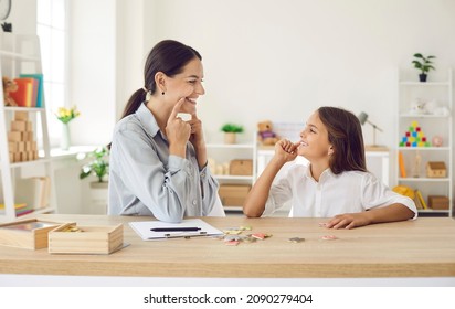 Female Specialist Working On Kid's Speech Impediments. Smiling Child Together With Professional Language Therapist Sitting At Desk In Modern Office, Playing Fun Games, Developing Correct Pronunciation