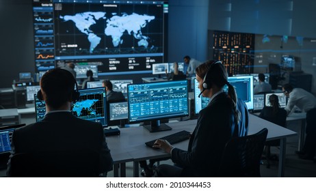 Female Specialist Works on a Computer with Live Ananlysis Feed from a Global Map on a Big Digital Screen. Employees Sit in Front of Displays with Financial Stock Market Trading Info and Big Data. - Powered by Shutterstock