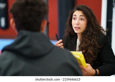 Female Sports Psychologist With Pen And Folder Speaking With Male Athlete During Motivational Session In Contemporary Gym