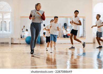 Female sports teacher running with her students during physical education class at school gym. Copy space.  - Powered by Shutterstock