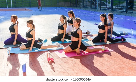 Female Sports Team Of Attractive Slender Girls Doing Pilates Exercises On Special Mats On The Outdoor Stadium In The Urban Park. Healthcare And Active, Sports Lifestyle Concept.