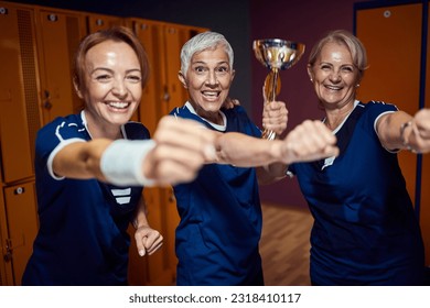 Female sports team of three celebrating together in locker room, holding golden cup. Senior team winning. - Powered by Shutterstock