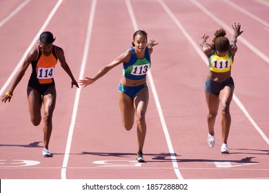 Female sprinters crossing the finish line at the end of a sprint race on a bright, sunny day at the track