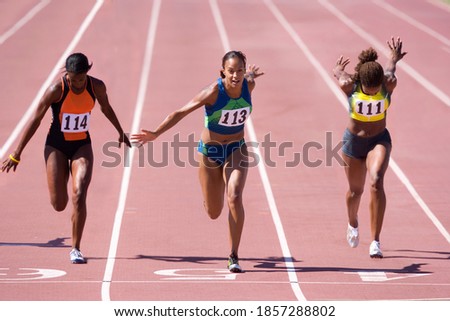 Female sprinters crossing the finish line at the end of a sprint race on a bright, sunny day at the track