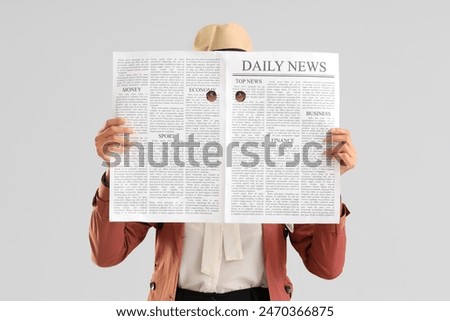 Female spy with newspaper on light background
