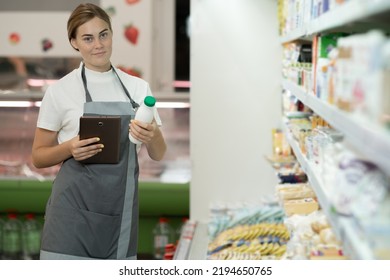 female staff in apron using digital tablet in supermarket holding a bottle of milk in his hands, copy space - Powered by Shutterstock