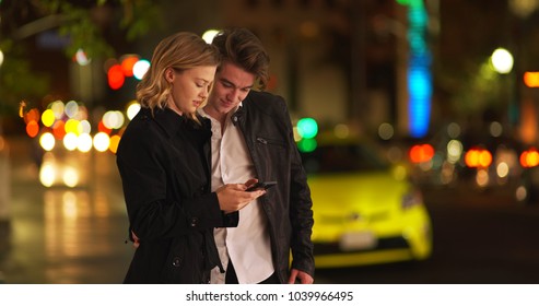 Female standing with boyfriend on city street in evening messaging