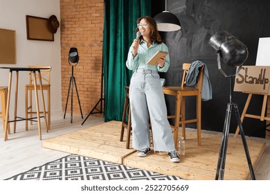 Female standup comedian with microphone and notebook performing on stage - Powered by Shutterstock