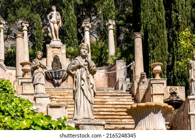 Female statue in front of a staircase called Apollo Staircase lined with gargoyles and amphorae next to cypresses and ivy leads to a monument of god Apollo in Apollo garden of the public Raixa mansion