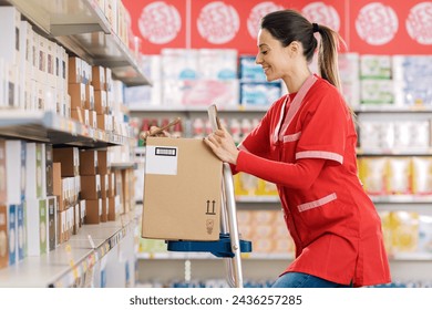 Female stock clerk working at the supermarket, she is standing on a ladder and smiling - Powered by Shutterstock