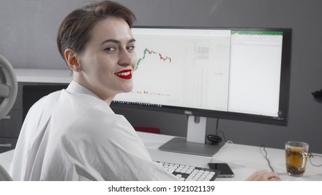 Female Stock Trader Smiling To The Camera While Working On Her Computer