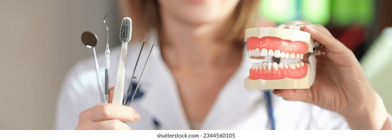 Female stomatologist shows dentist tools and toothbrush in one hand and jaws with teeth in another. Dental clinic and healthcare concept. - Powered by Shutterstock