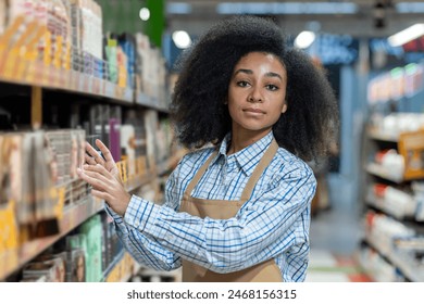 Female store employee wearing an apron organizing products on a supermarket shelf, showcasing grocery store work and retail management. - Powered by Shutterstock