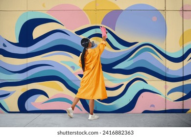 Female street artist painter in respirator mask painting colorful graffiti on wall Modern art, urban concept.