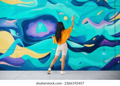 Female street artist painting bright colorful graffiti on wall. Modern art, urban concept. Full length portrait - Powered by Shutterstock