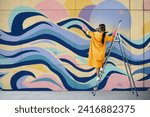 Female street artist painting colorful graffiti standing on a ladder. Modern art, urban concept.