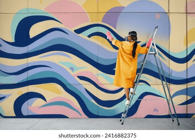 Female street artist painting colorful graffiti standing on a ladder. Modern art, urban concept.
