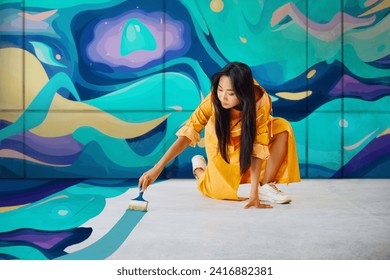 Female street artist painting colorful graffiti on the ground with copy space Modern art, urban concept.