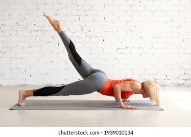 Female Strength Training Without Props. Attractive Athletic Caucasian Woman Does Push Ups With One Leg Up In Loft White Studio, Indoor Workout, Selective Focus.